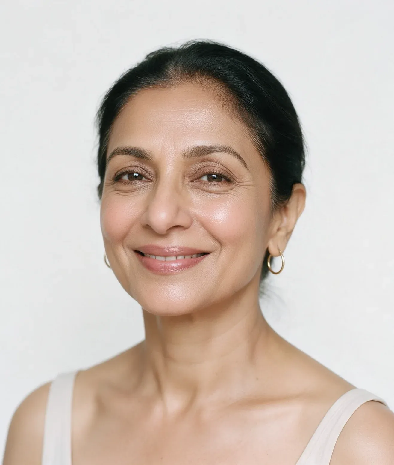 Studio portrait of a smiling woman in her fifties with a dewy glow on her cheekbones